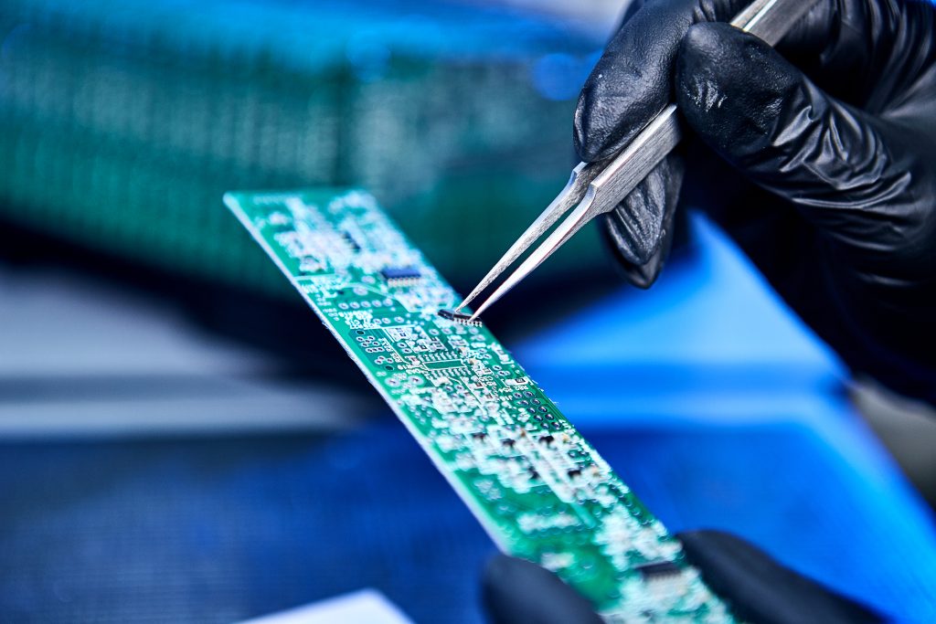 Componente eletrônico sendo inserido manualmente em placa PCB com pinça de precisão